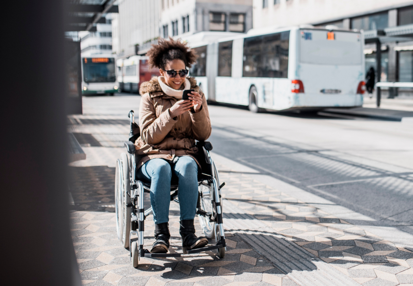 person in a wheelchair waiting for a bus while looking at their phone